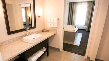 A hotel bathroom with a sink, mirror, towel rack, and a view of a bedroom with a bathtub.