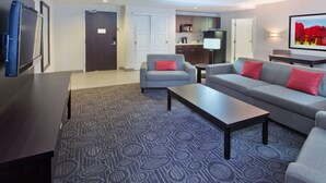 A modern living room with a grey sofa, a coffee table, and a TV. There is a kitchen area with cabinets and a microwave. - Holiday Inn Hotel & Suites Red Deer South by IHG (Red Deer)