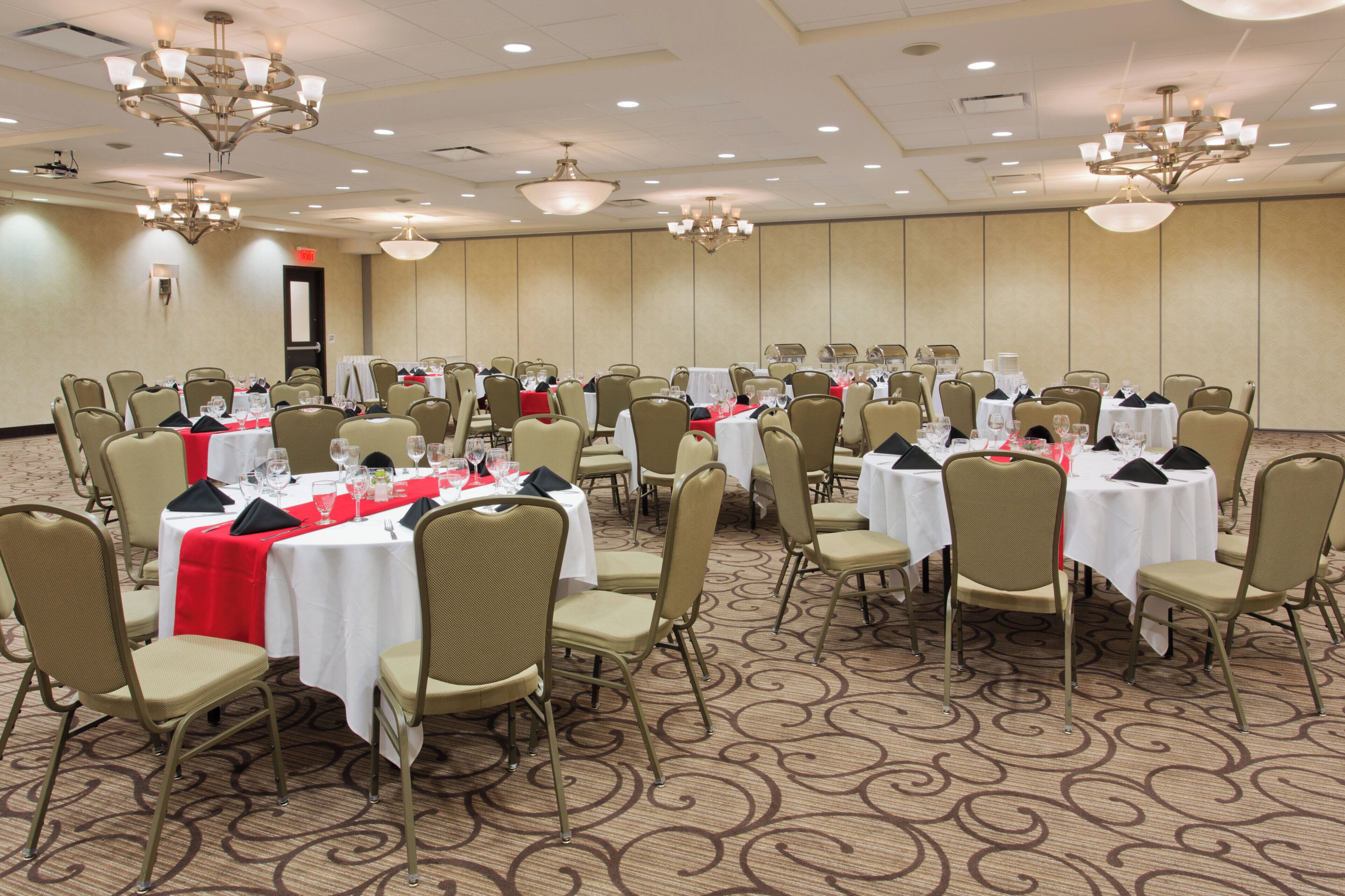 A banquet hall with round tables, chairs, and chandeliers.