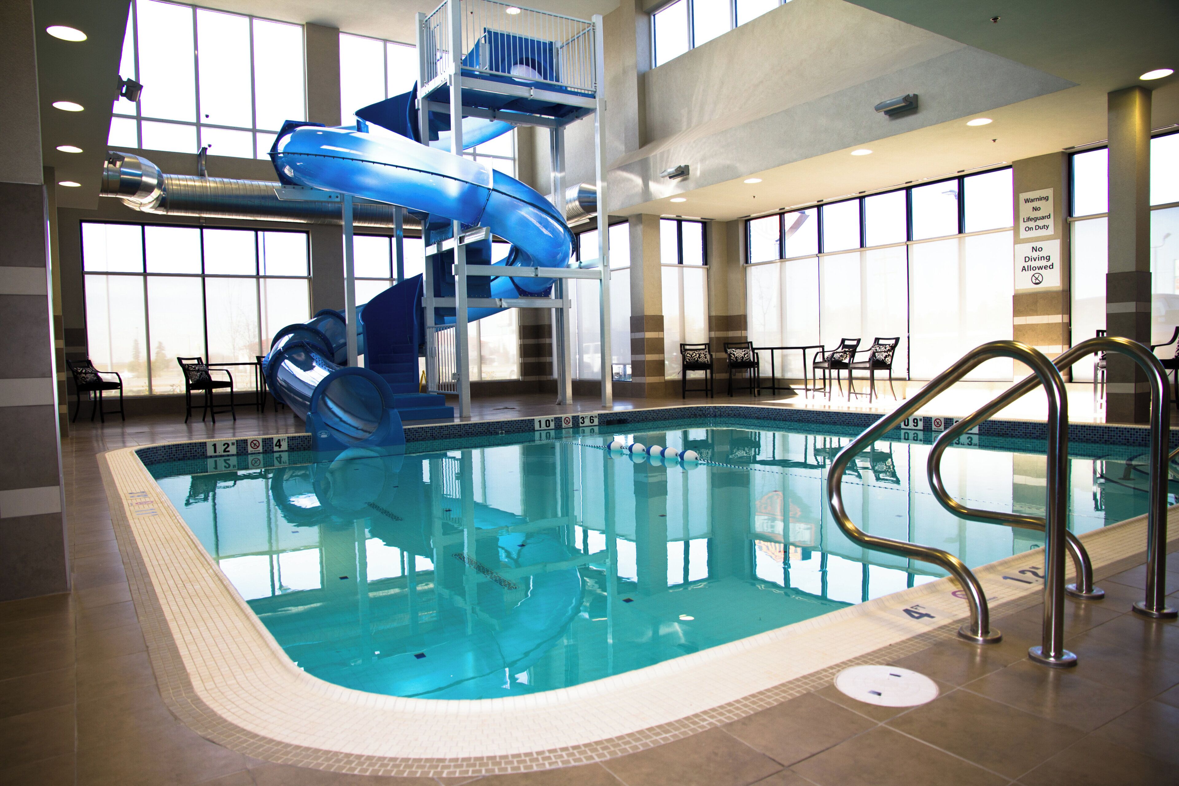 Ein Hallenbad mit blauem Wasserrutschen, gut sichtbaren Beckenrändern und einem Rettungsschwimmerstand.