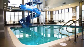 Ein Hallenbad mit blauem Wasserrutschen, gut sichtbaren Beckenrändern und einem Rettungsschwimmerstand.
