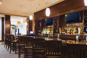 Un área de bar con diversas opciones de asientos, una pantalla de televisión y una variedad de botellas en los estantes.