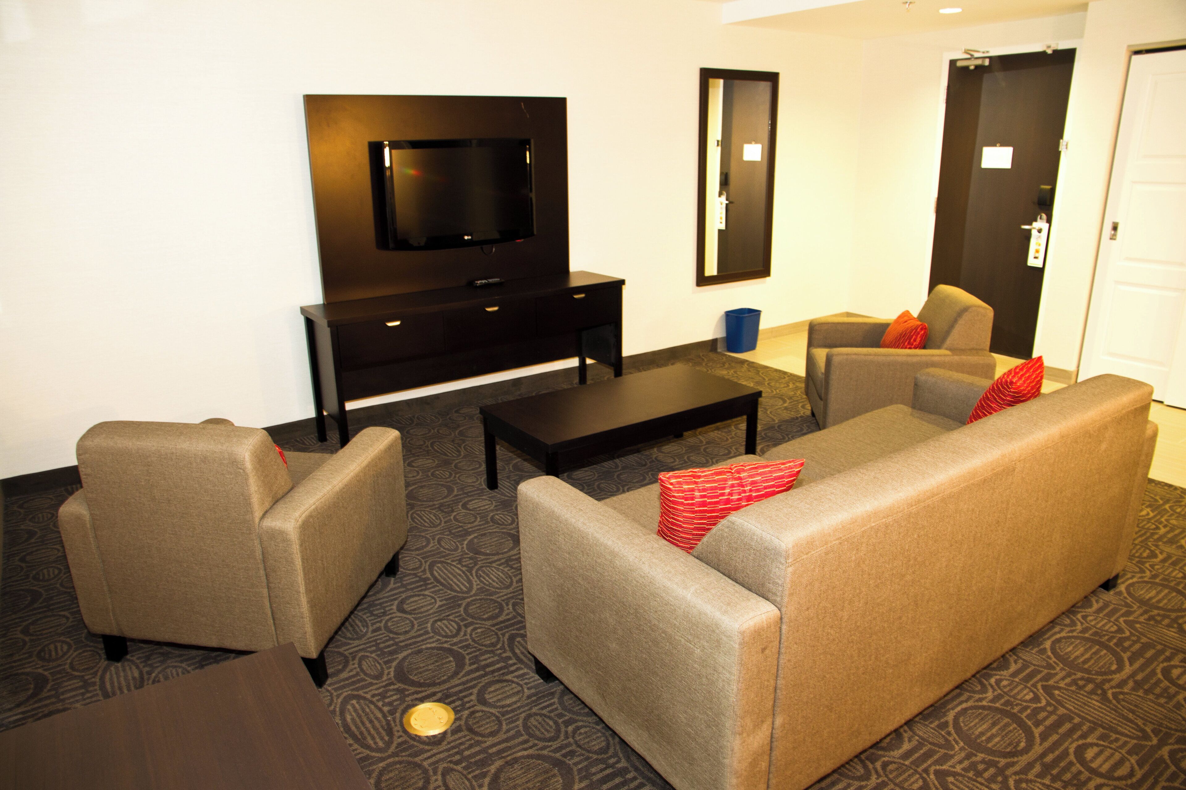 Habitación de hotel con sofá, sillones, una mesita de centro, televisor de pantalla plana y una pequeña mesita auxiliar.