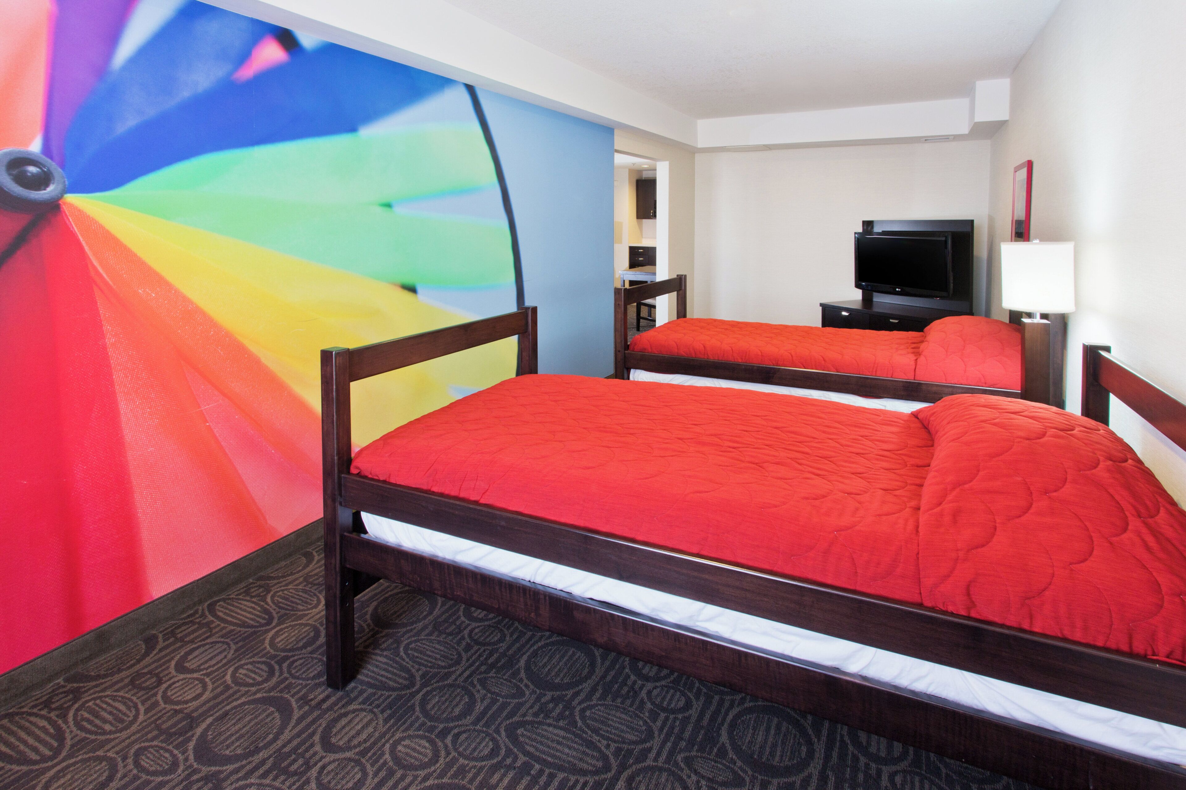 A hotel room with two beds, a television, and a colorful mural on the wall.