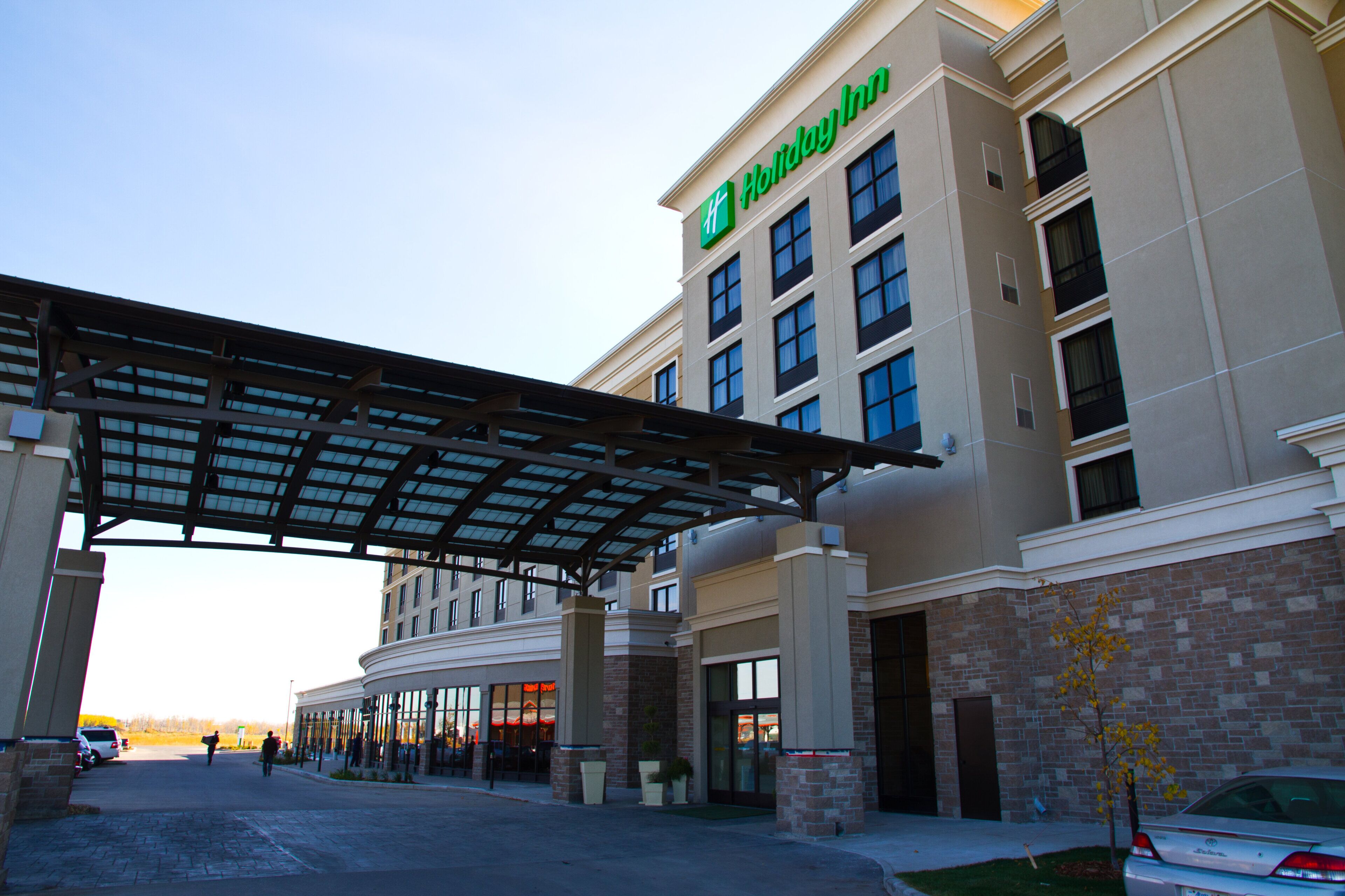 A Holiday Inn hotel with a covered entrance, brick facade, and a clear sky.