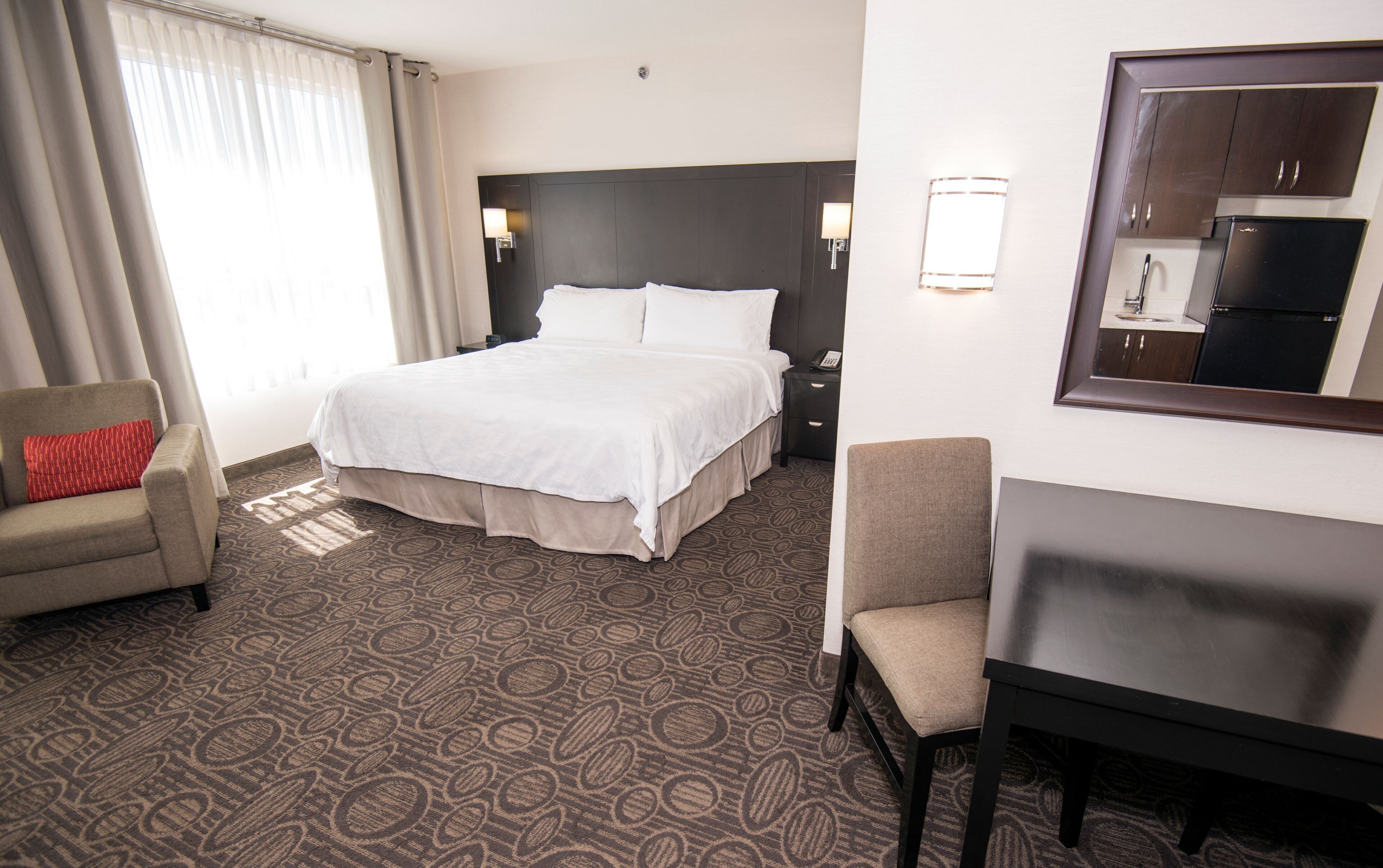 Una habitación de hotel con cama, escritorio, silla, mesita de noche y espejo.