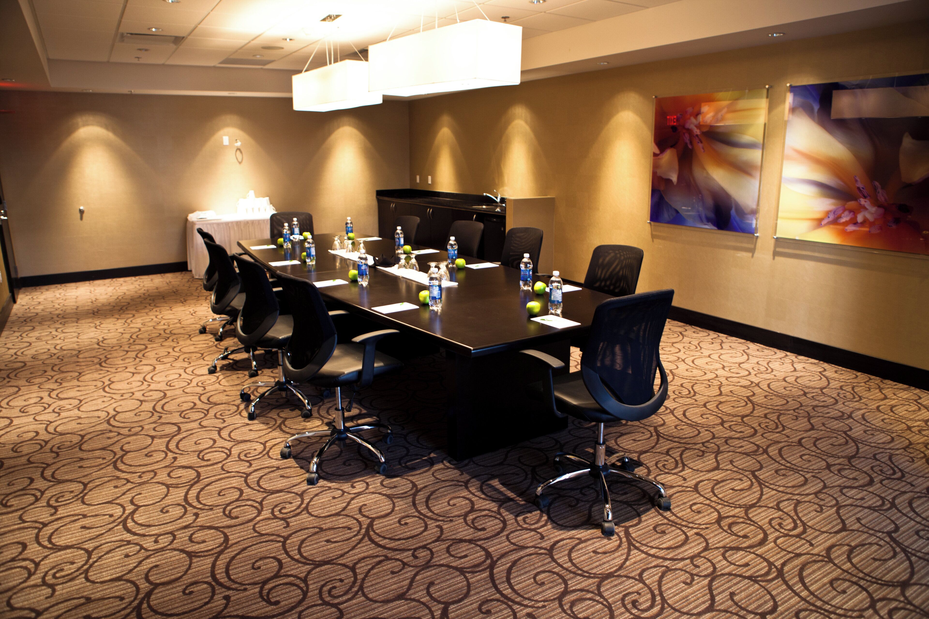 A conference room with a long table, chairs, water bottles, and a projector screen.