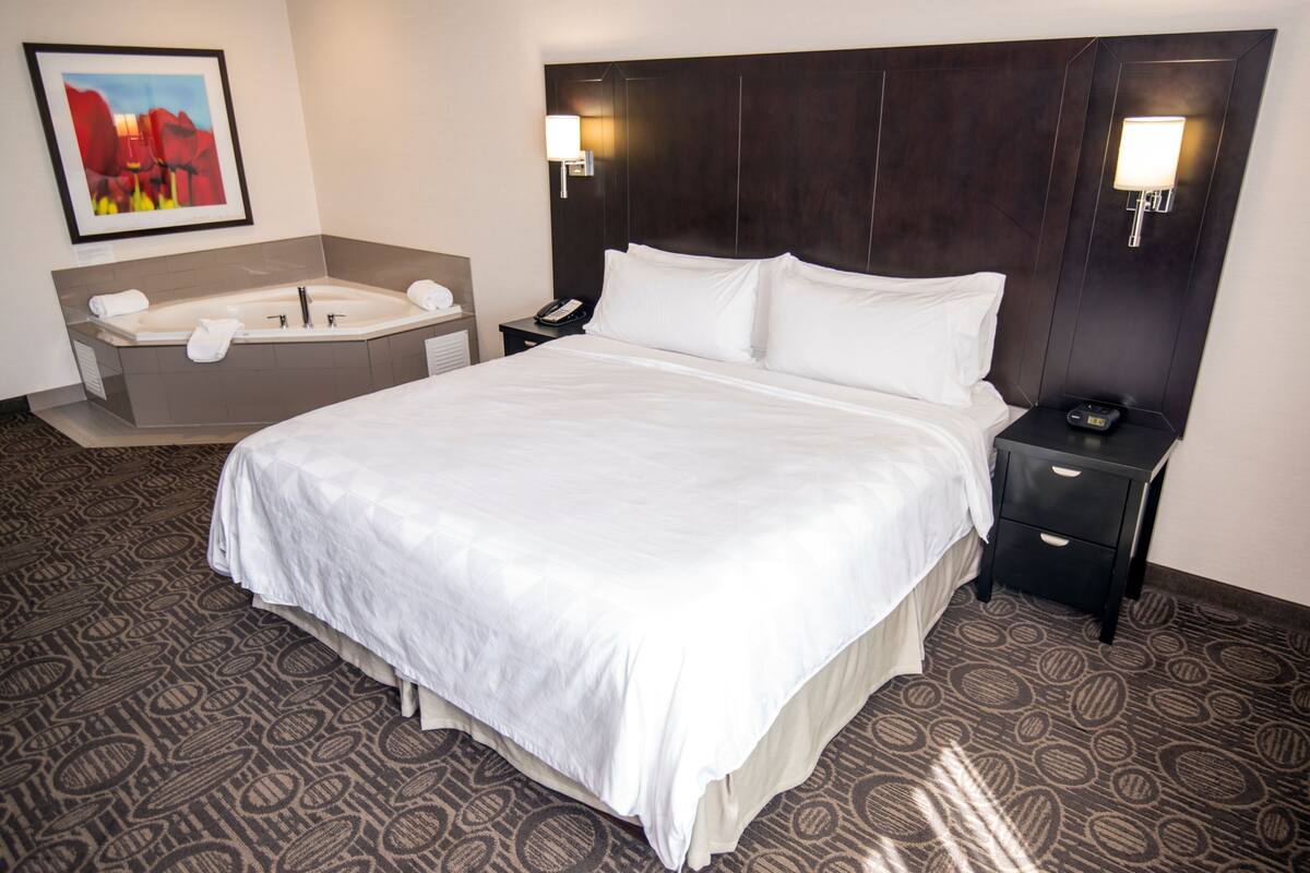 A hotel room with a large bed, a separate bathroom with a bathtub, and a nightstand with a phone and lamp.