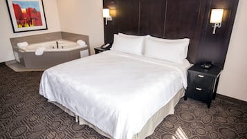 A hotel room with a large bed, a separate bathroom with a bathtub, and a nightstand with a phone and lamp.