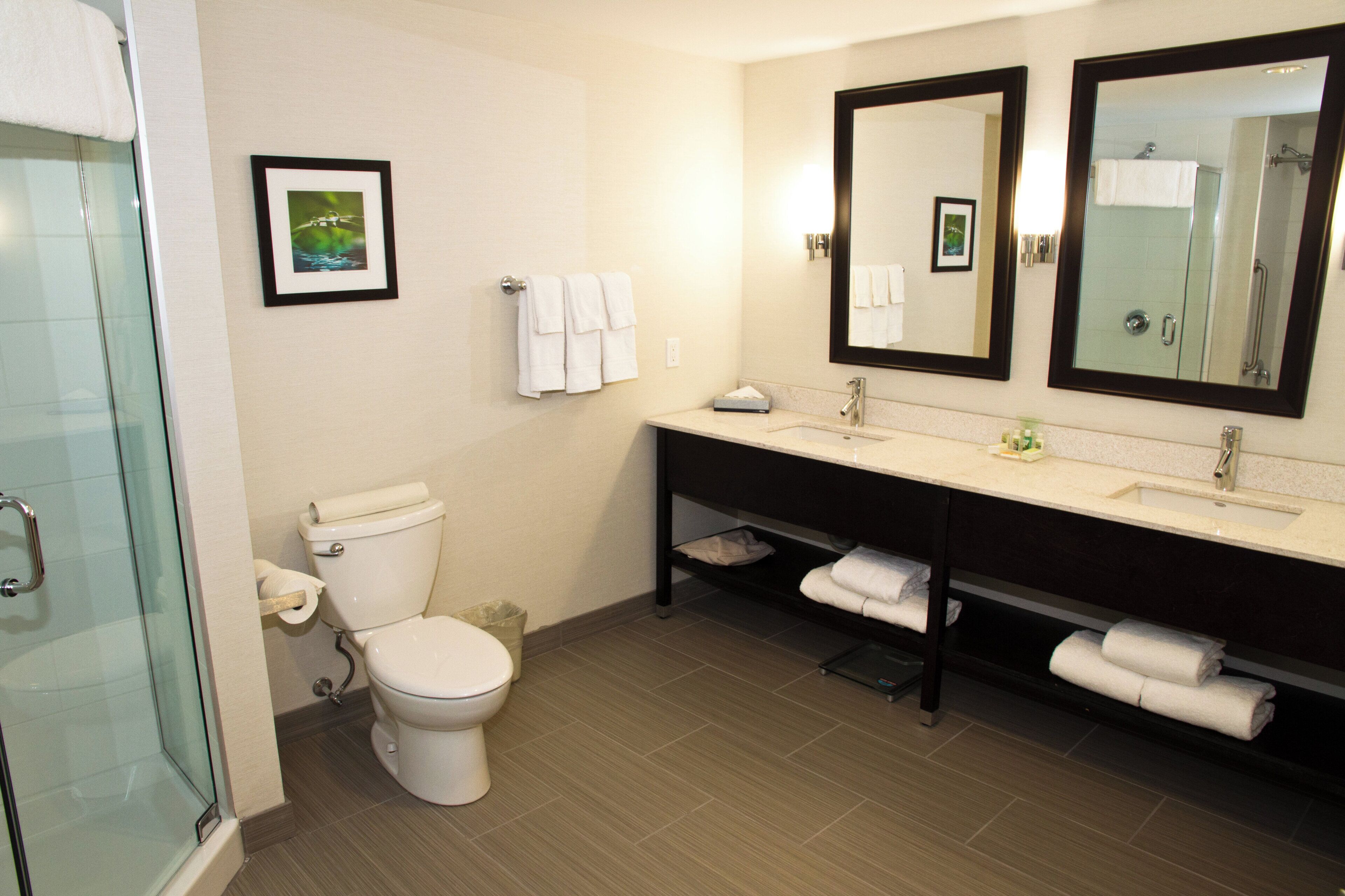 A modern bathroom with a toilet, sink, and shower. There are towels and a framed picture on the wall.