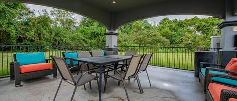 An outdoor patio with a table and chairs, surrounded by wicker furniture and a grill.