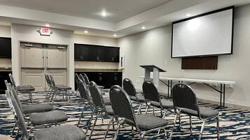 A conference room with a projector screen, a white table, and multiple chairs arranged for meetings.