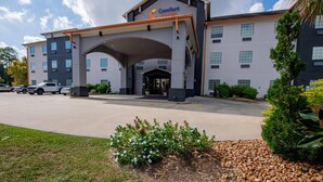 A Comfort Suites hotel with a modern design, featuring a large entrance canopy, multiple windows, and a parking lot with several cars. - Comfort Suites Oil Center (Lafayette)