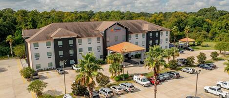A Comfort Suites hotel with a parking lot, multiple buildings, and surrounding greenery.