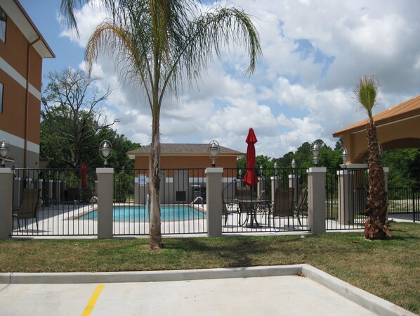 A gated pool area with a pool, chairs, and umbrellas.