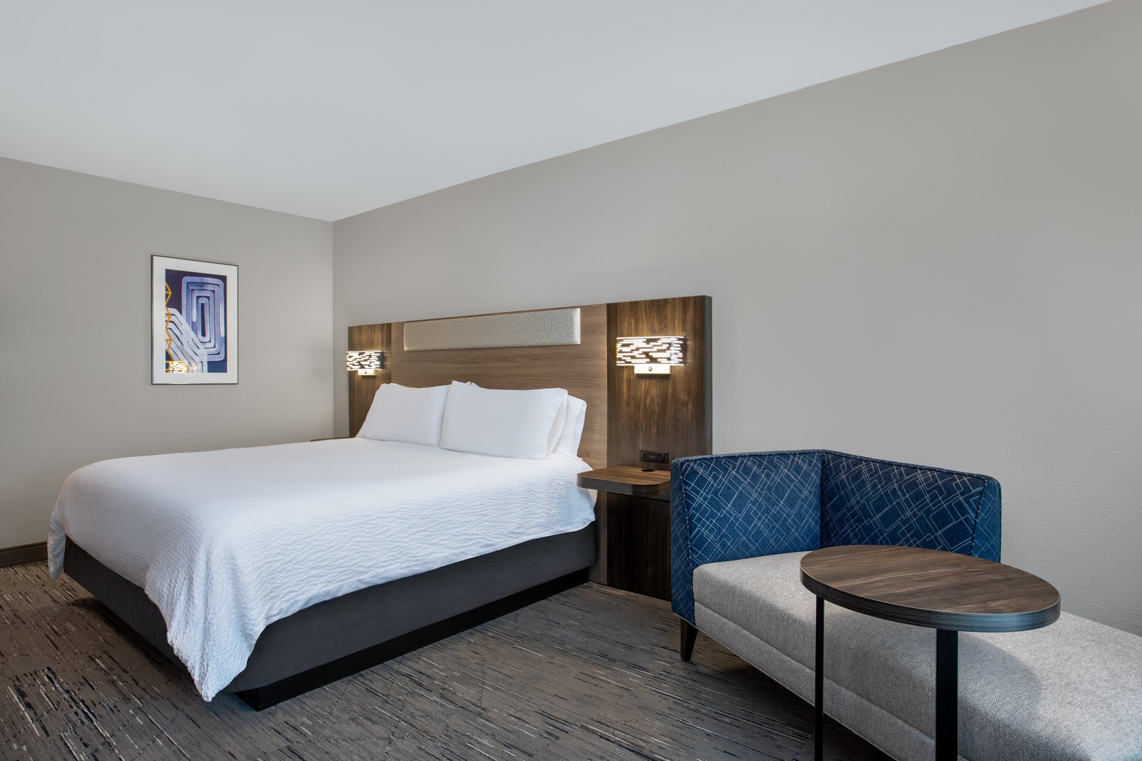 Una habitación de hotel con una cama, una mesita de noche, una silla y una pequeña mesa.