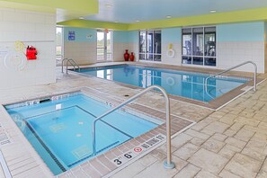 A swimming pool with clear lane markings and safety signs, a tiled floor, and a door leading to a changing room. - Holiday Inn Express & Suites Terre Haute by IHG (Terre Haute)