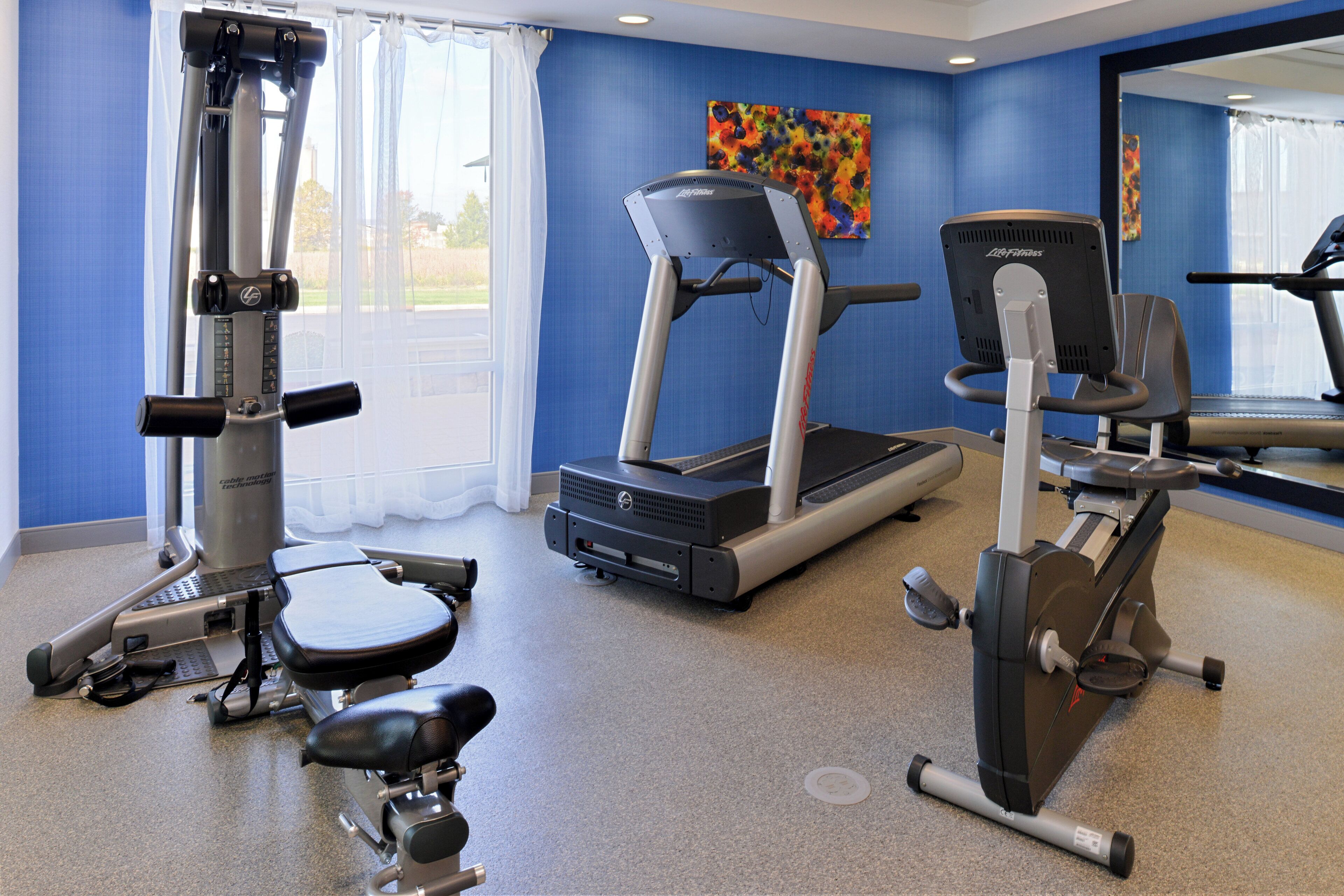 Un gimnasio con máquinas de cardio, una banca y un espejo.