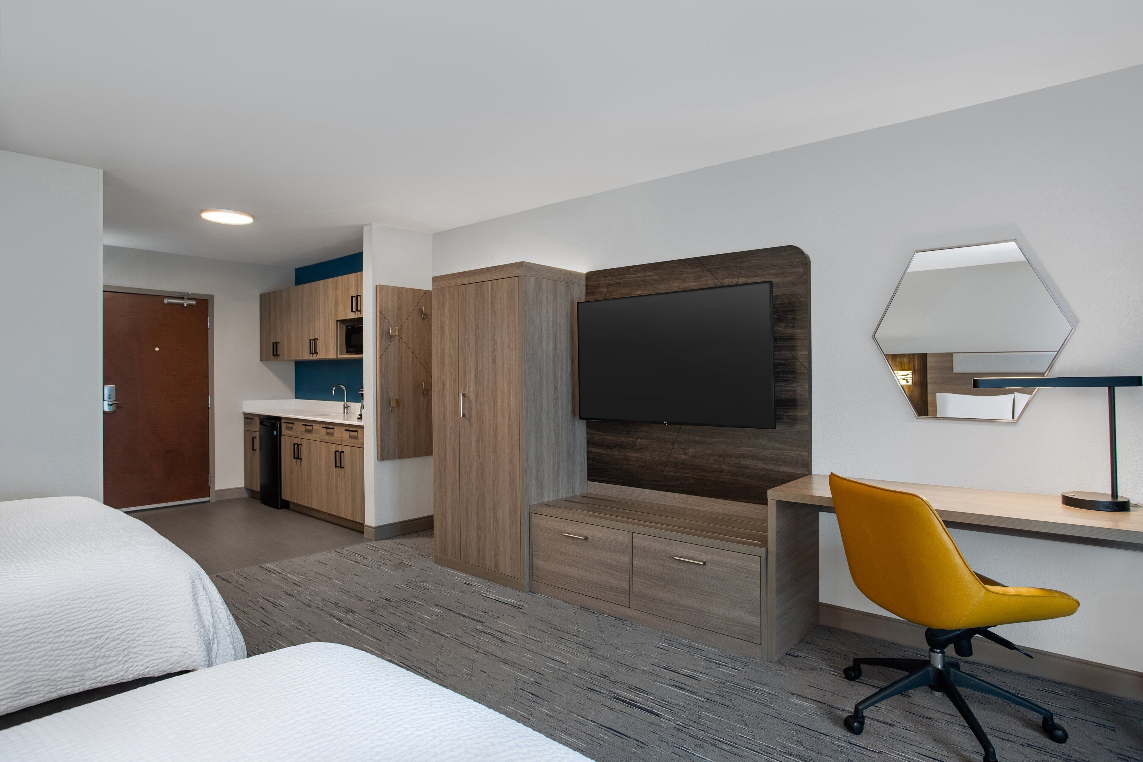 Moderni hotellihuone, jossa on sänky, työpöytä tuolilla, televisio ja pieni keittiönurkkaus.