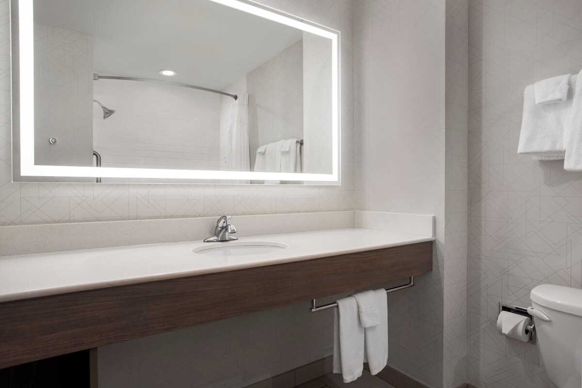A modern bathroom with a large mirror, white sink, and a towel rack.