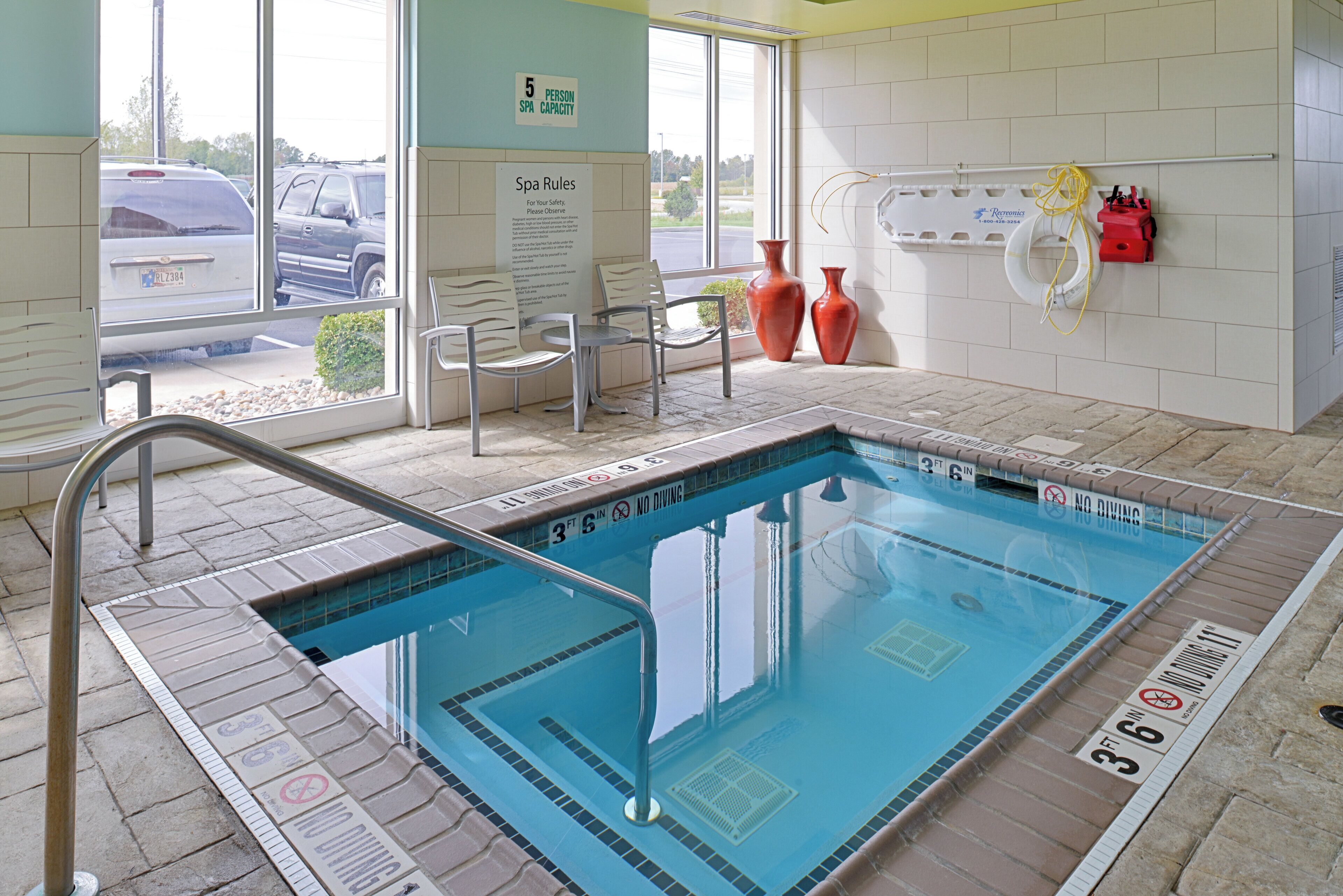 A swimming pool with a 5-person spa capacity sign, a chair, and a lifebuoy on the wall.
