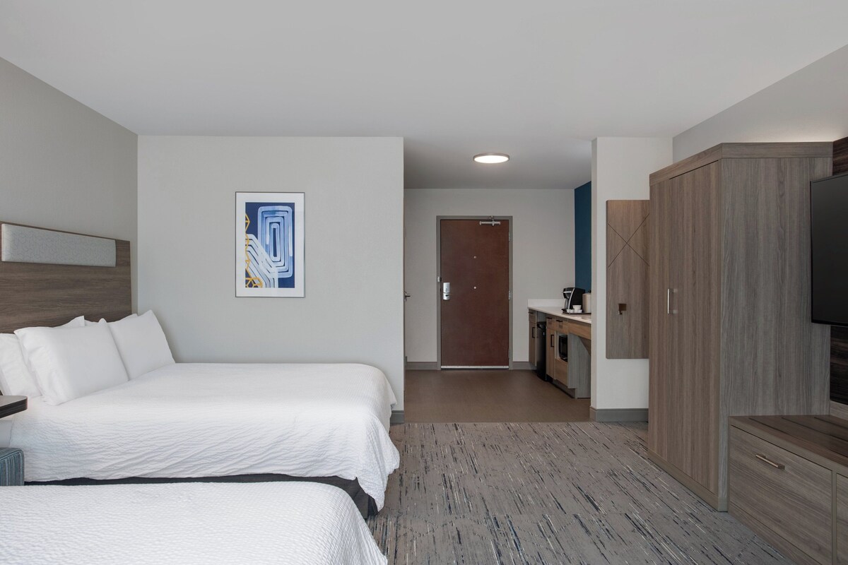 A hotel room with two beds, a wooden wardrobe, a desk with a chair, and a television.