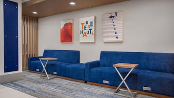 A modern waiting area with two blue sofas, a wooden table, and three framed artworks on the wall.