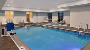A modern indoor swimming pool with clear lane markings, a changing room, and a seating area with chairs.