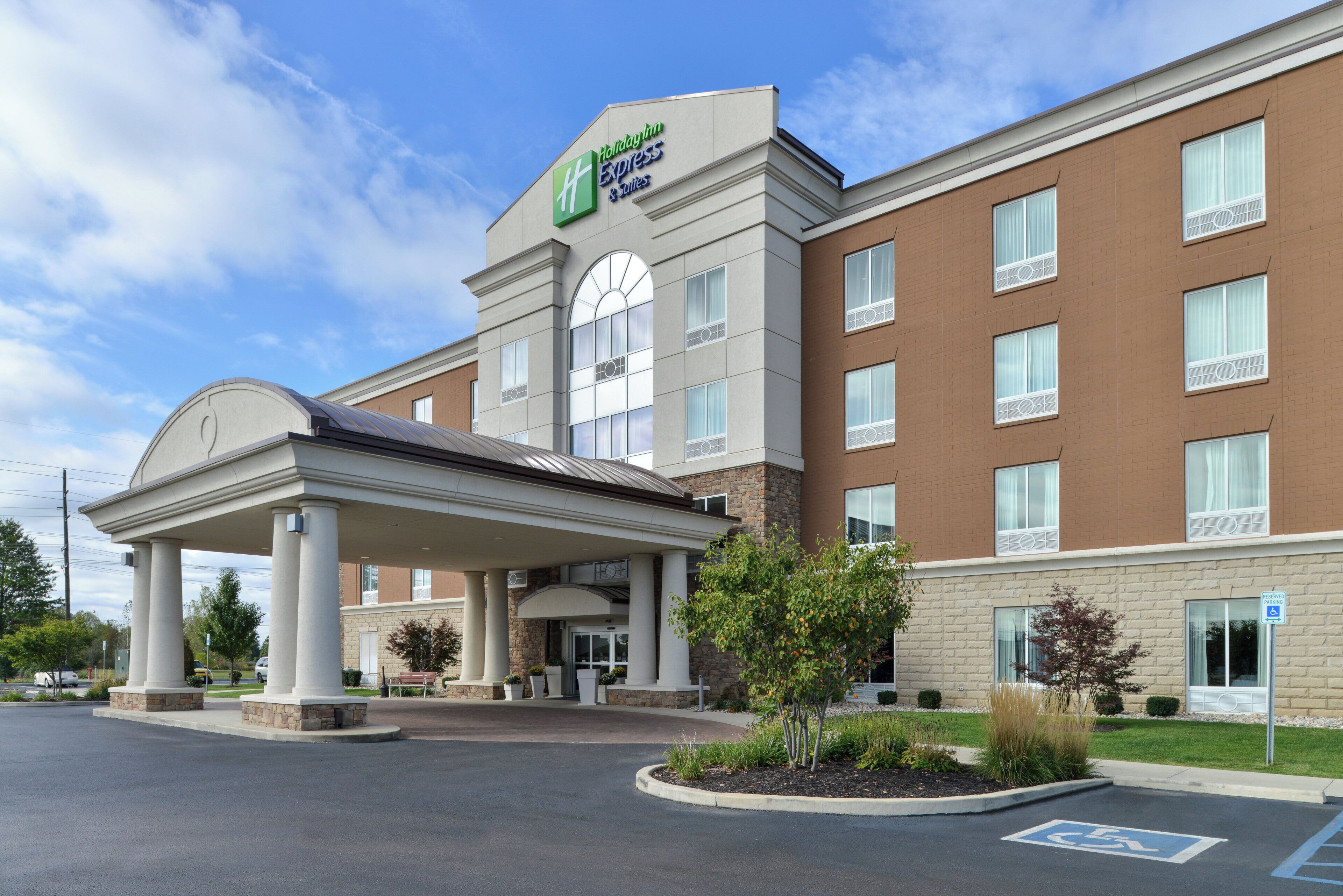 Un hotel Holiday Inn Express & Suites con entrada cubierta, múltiples ventanas y un estacionamiento que incluye señal de estacionamiento para discapacitados.