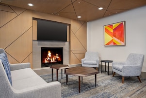 Uma sala de estar moderna com lareira, dois poltronas cinzas, um sofá e uma mesa de centro.