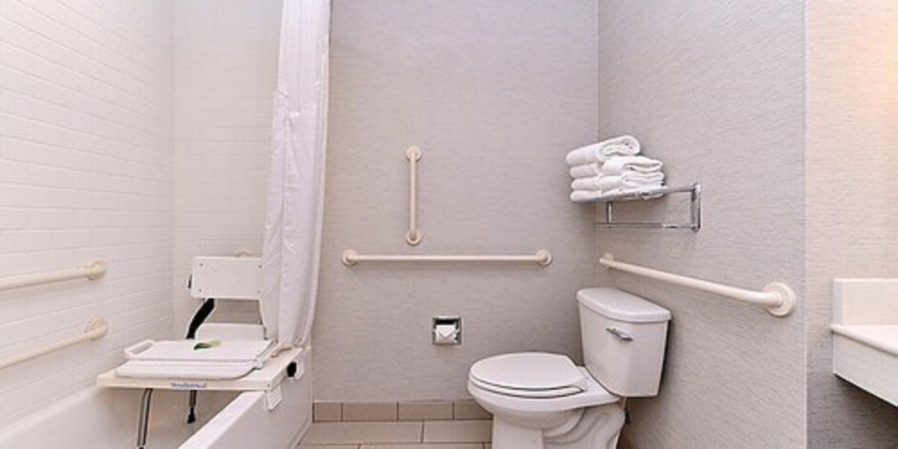 Een badkamer met een wit toilet, een douche met een witte gordijn en handgrepen aan de muur.