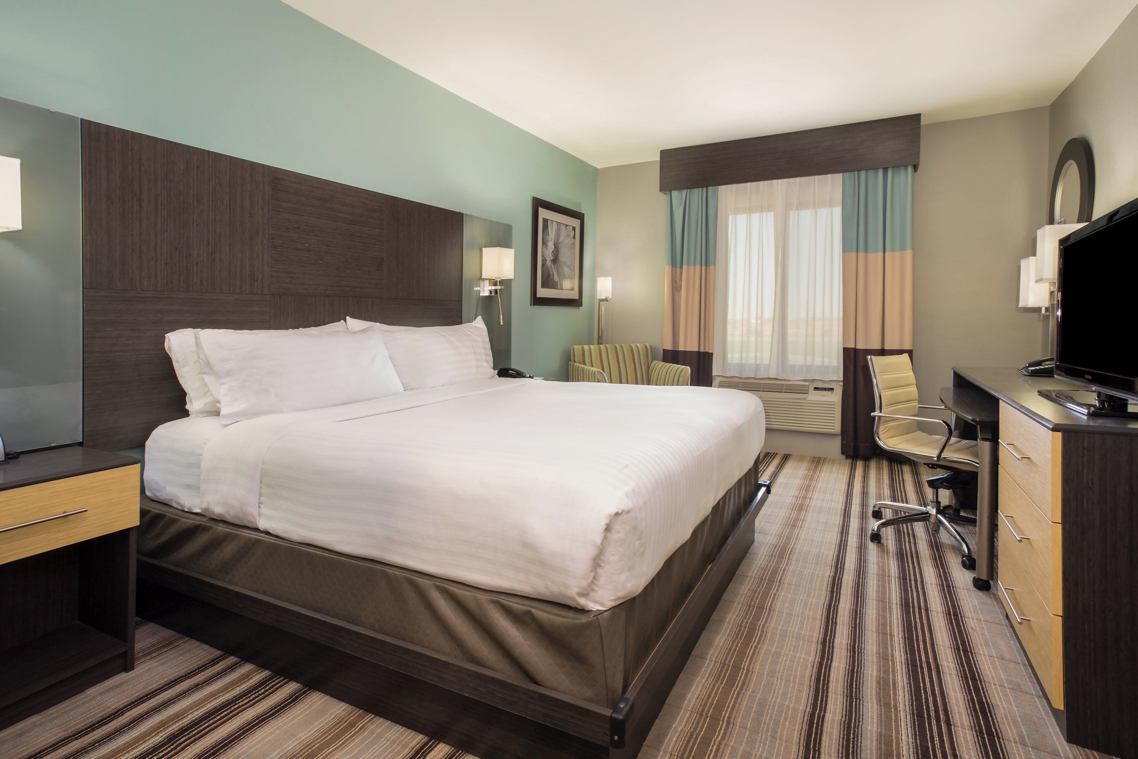 A hotel room with a large bed, a desk, a chair, a television, and a window with curtains.