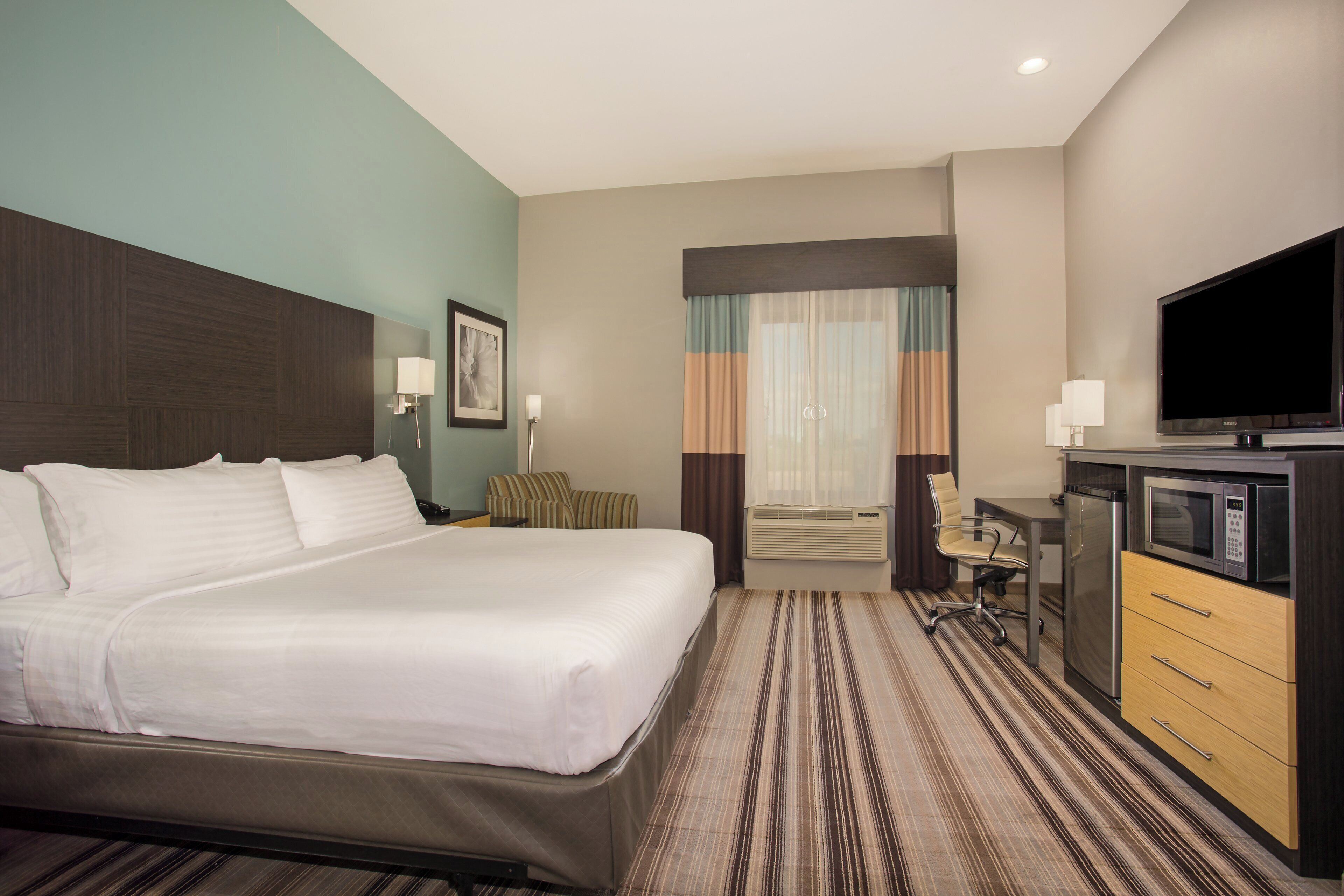 Una habitación de hotel con una cama grande, un escritorio con computadora, televisor y microondas.