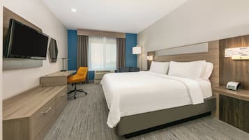 A hotel room with a large bed, a desk, a chair, a TV, and a bedside table.