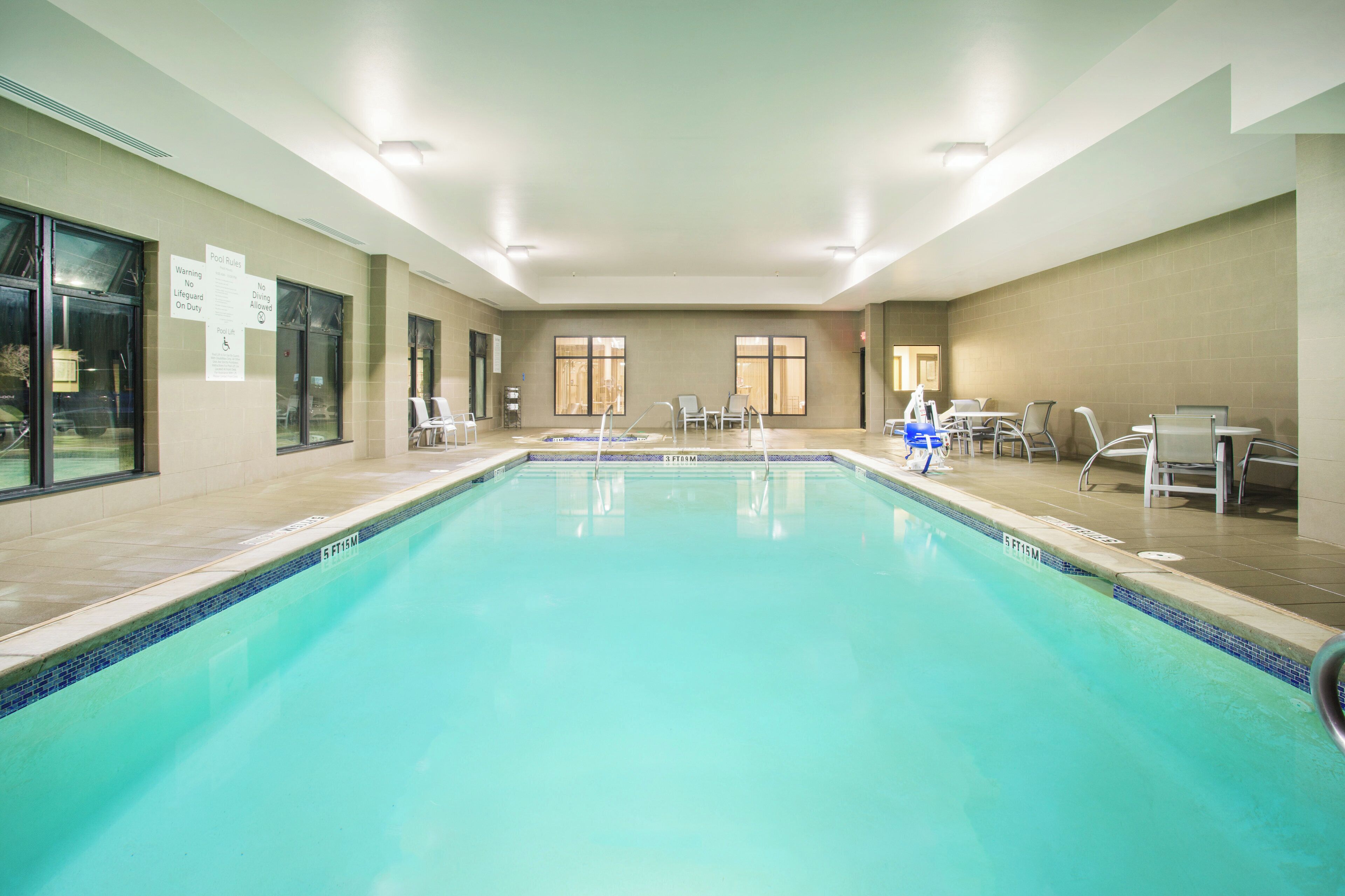 A large indoor swimming pool with clear water, surrounded by lounge chairs and tables, and a sign indicating no diving allowed.