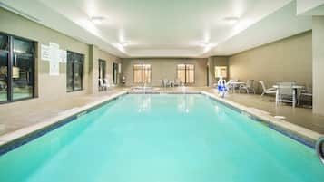 A large indoor swimming pool with clear water, surrounded by lounge chairs and tables, and a sign indicating no diving allowed.