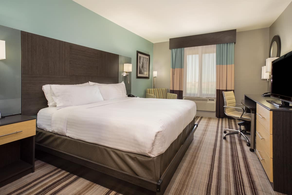 Ein Hotelzimmer mit einem großen Bett, einem Schreibtisch mit Stuhl, einem Fernseher und einem Fenster mit Vorhängen.