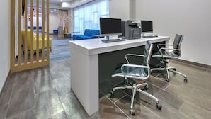 Un espacio de oficina moderno con un escritorio blanco, dos monitores, una impresora y sillas ergonómicas.