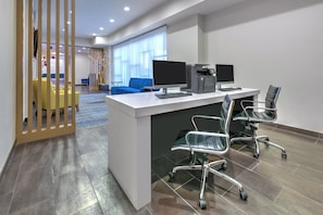 Un espacio de oficina moderno con un escritorio blanco, dos monitores, una impresora y sillas ergonómicas.