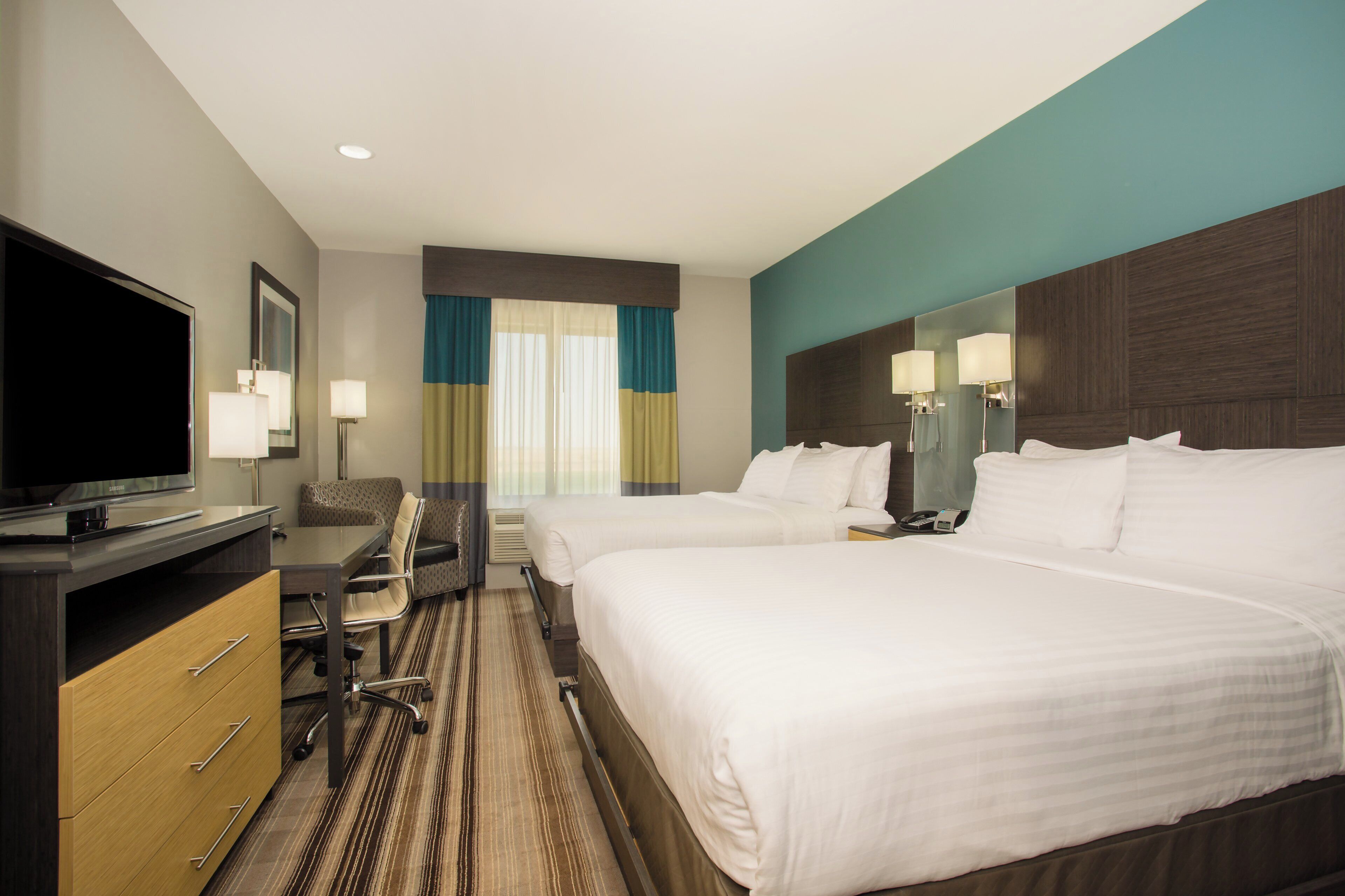 Quarto de hotel com duas camas, uma escrivaninha, televisão e espelho no banheiro.