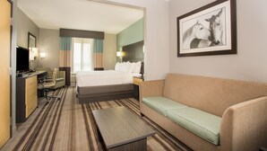 Habitación de hotel con cama, sofá, escritorio con silla, televisor y un cuadro en la pared.
