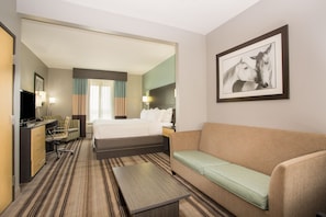 Habitación de hotel con cama, sofá, escritorio con silla, televisor y un cuadro en la pared.