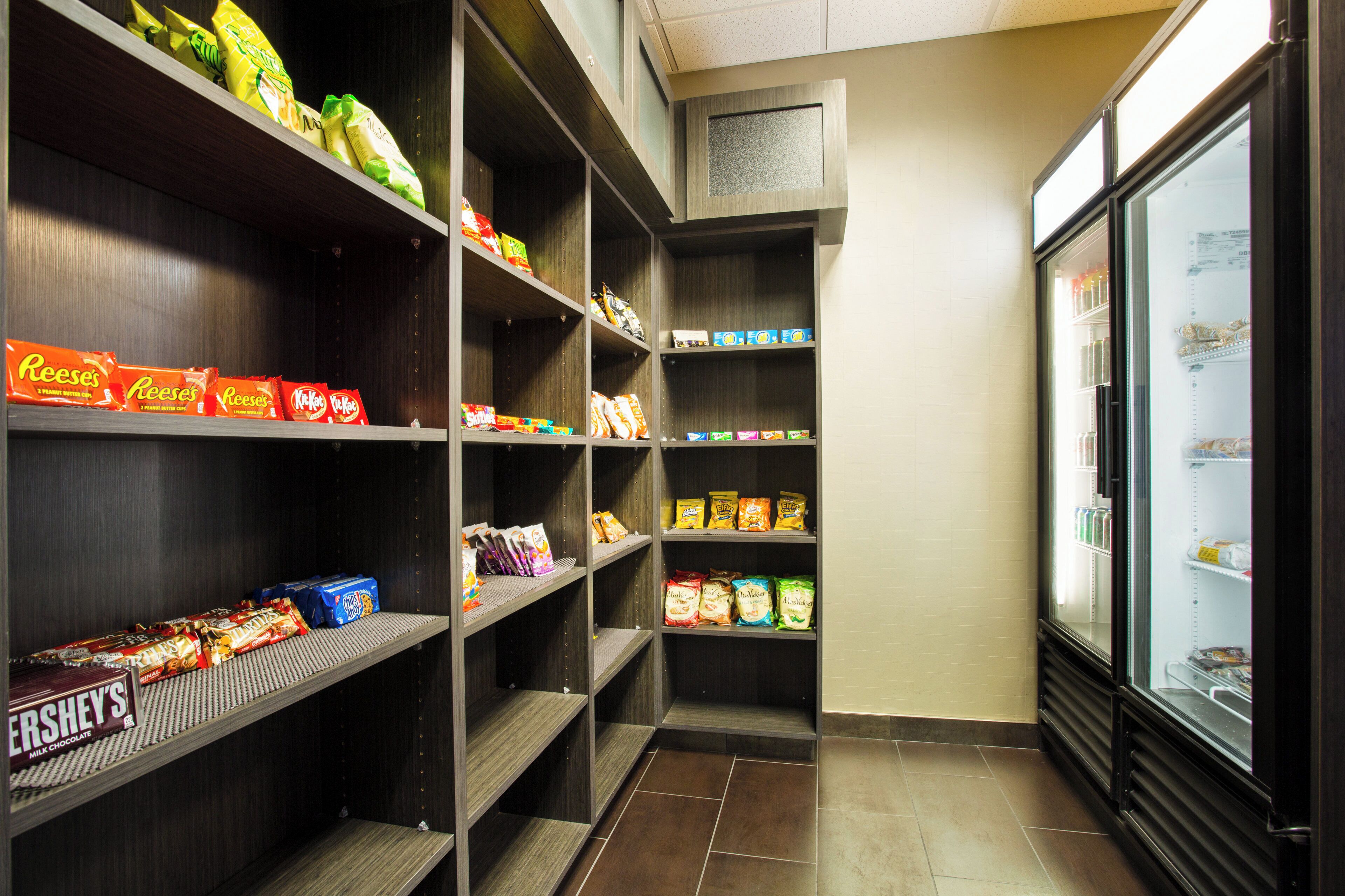 En sektion i en butik med snacks og drikkevarer, med hylder fyldt med forskellige snacks og et køleskab.