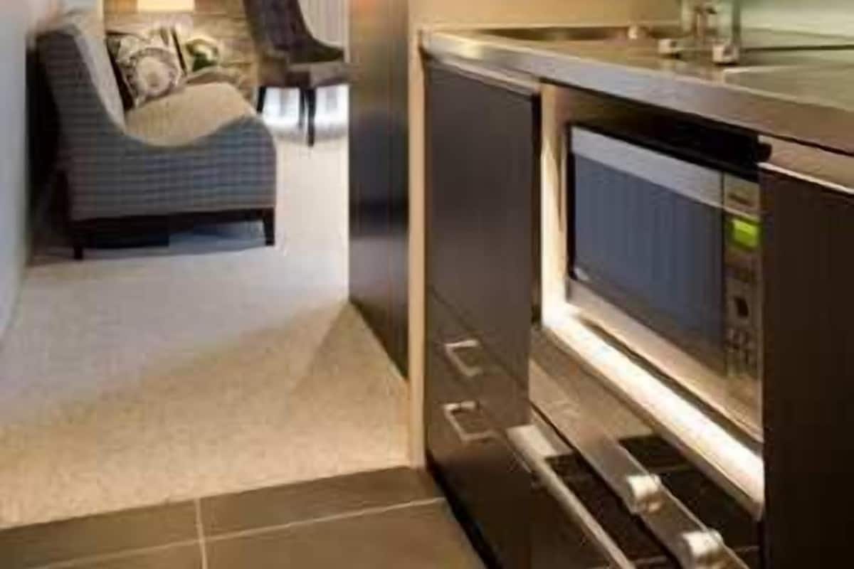 Eine moderne Küche mit Edelstahlgeräten, eine Sitzecke mit einer Couch und Sesseln sowie ein Blick in ein Wohnzimmer mit Lampe und Vorhängen.