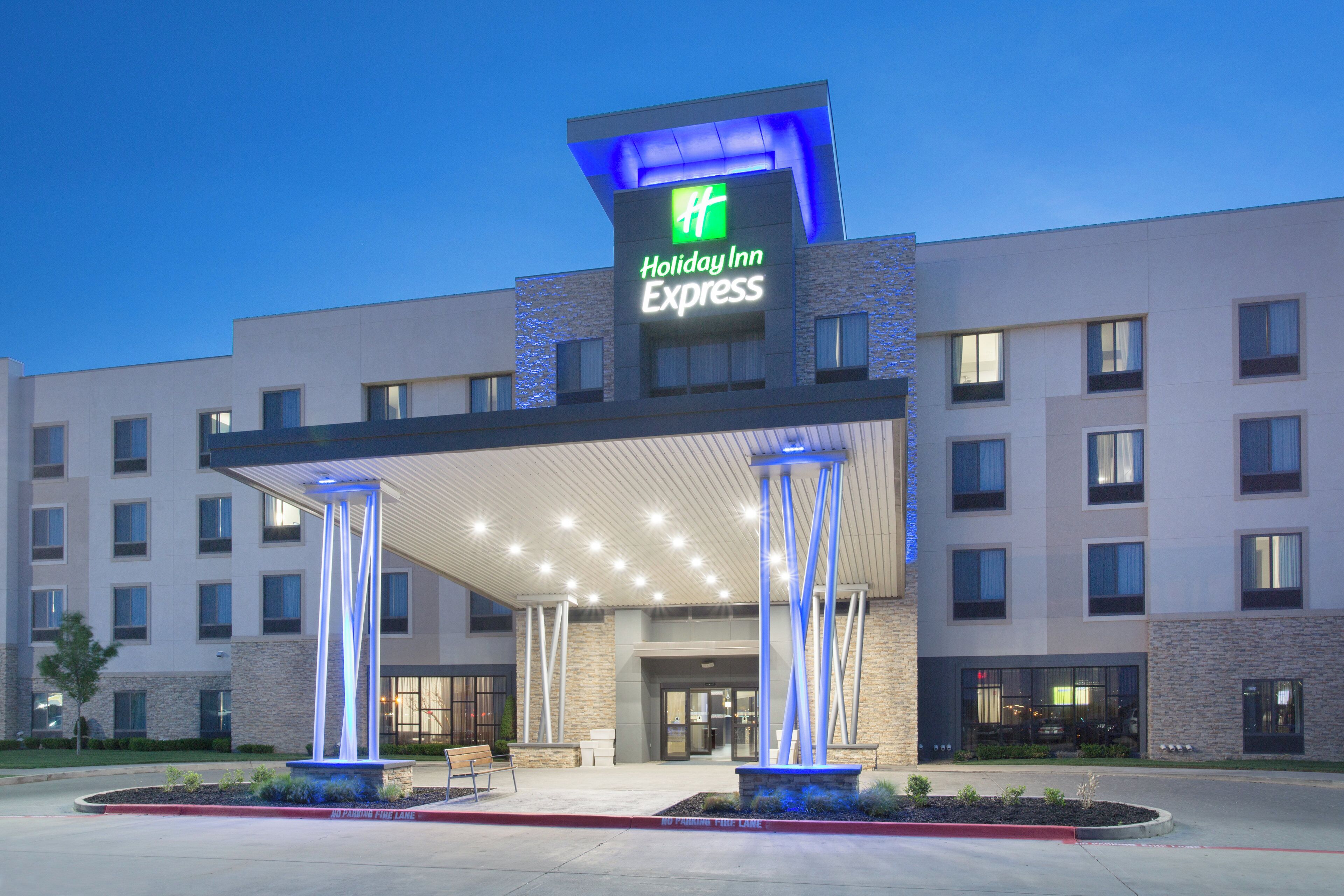 A Holiday Inn Express hotel with a covered entrance, multiple floors, and a landscaped area with a bench.