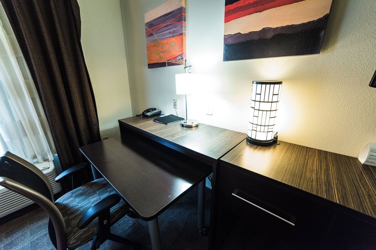 Una habitación de hotel con escritorio, silla, lámpara y cama.