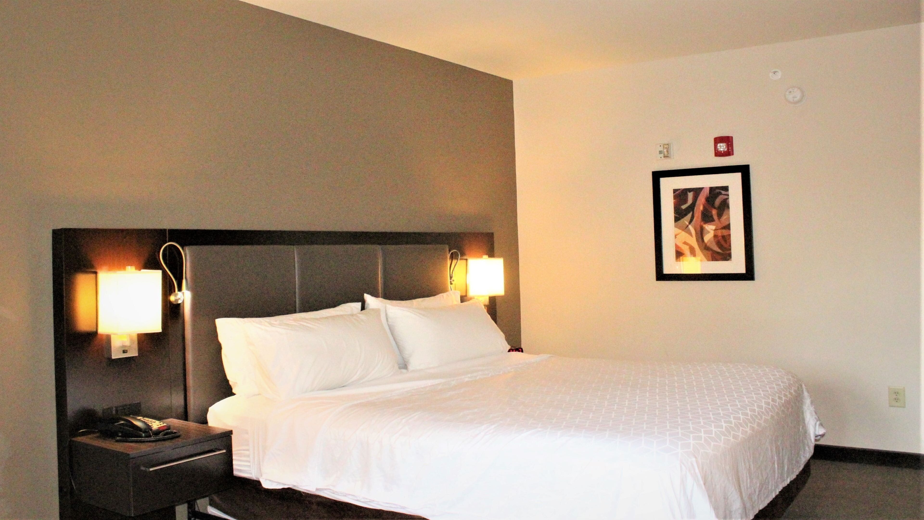 A hotel room with a bed, nightstand, and two wall-mounted lamps.