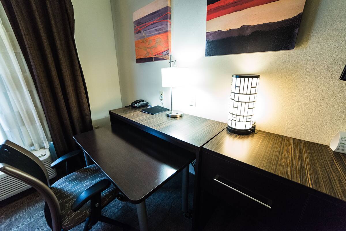 Ein Hotelzimmer mit einem Holztisch, einem Stuhl, einer Lampe und zwei Bildern an der Wand.
