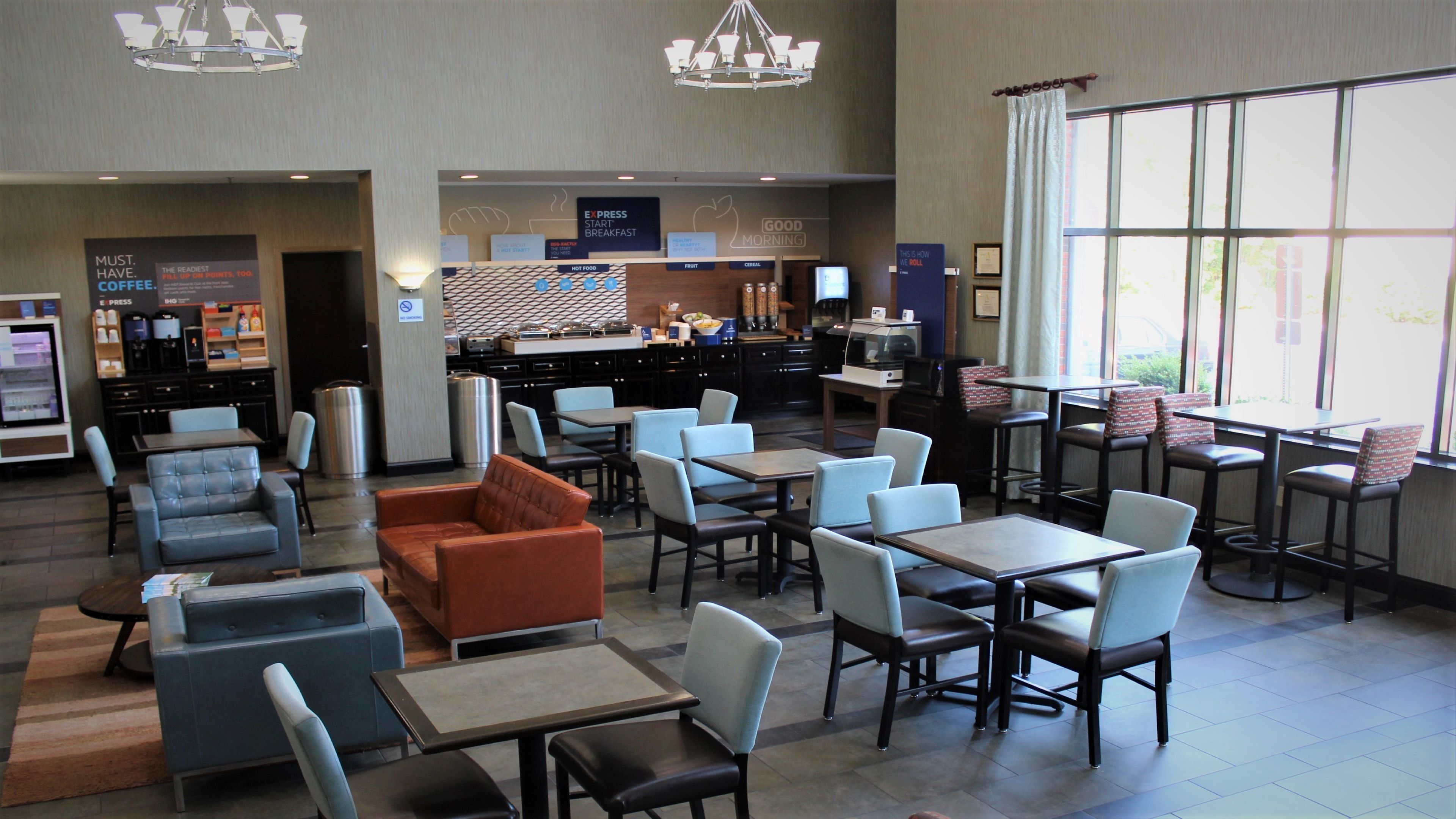 A hotel lobby with seating areas, a breakfast bar, and a large window providing natural light.