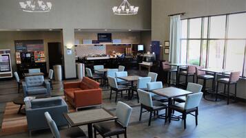 A hotel lobby with seating areas, a breakfast bar, and a large window providing natural light.